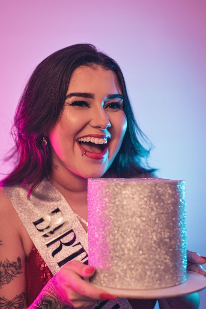 A woman joyfully holding a glittery birthday cake, wearing a sash. Perfect for party themes.