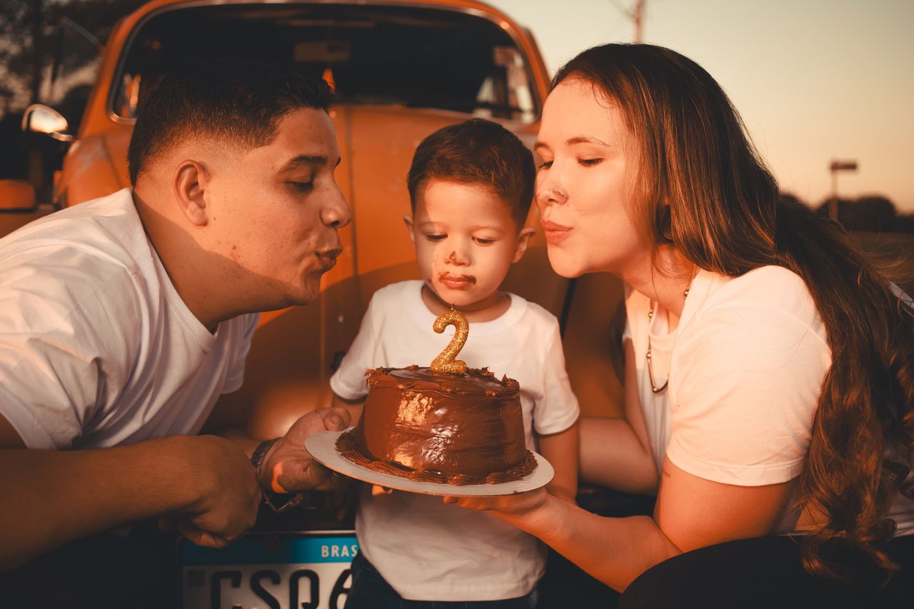 A family celebrating a child's second birthday outdoors with a cake.