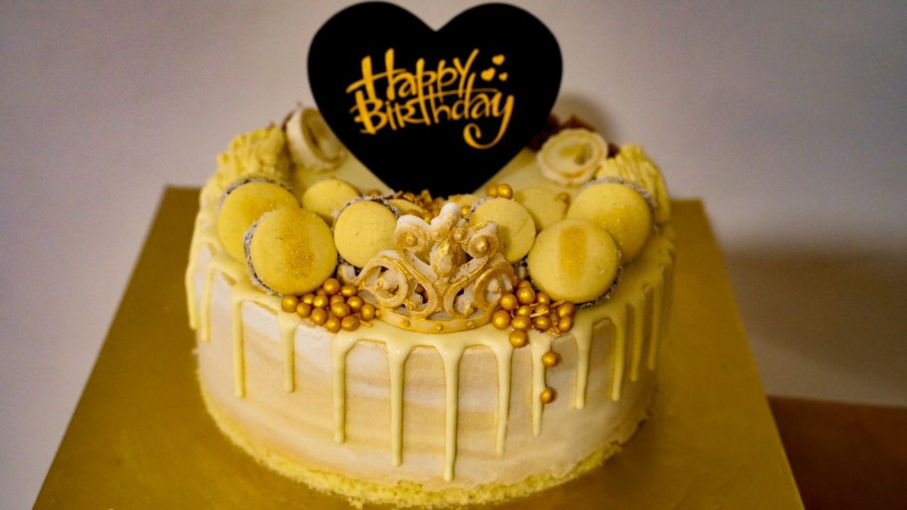 Stylish yellow birthday cake adorned with macarons and golden accents, perfect for celebrations.
